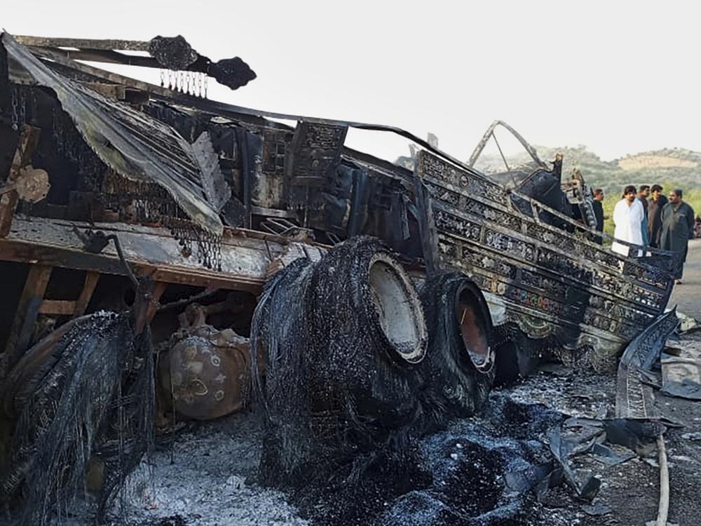 People look at a burnt vehicle which was torched by gunmen after they killed passengers at a highway in Musakhail, a district in Baluchistan province in restive southwestern Pakistan, Monday, Aug. 26, 2024.