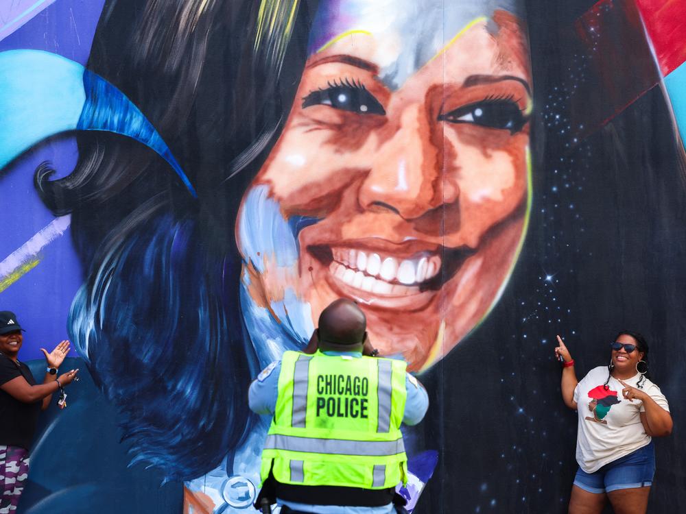 A Chicago police officer takes a picture of people posing before a mural of Vice President Kamala Harris outside the Democratic National Convention.