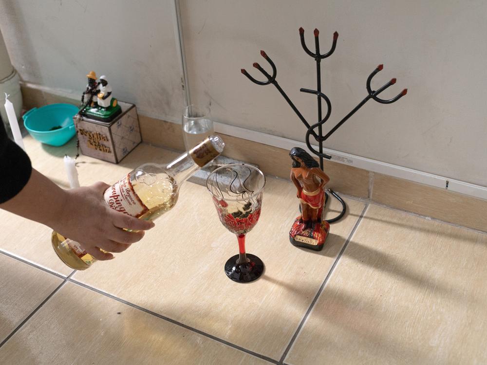 Érica Lacerda de Souza offers brandy to one of the spiritual entities in her home. Érica is a “mãe de santo.” a religious priestess of Umbanda, an Afro-Brazilian religion. Today, in her home, she and her husband practice Umbanda rituals and welcome other believers.