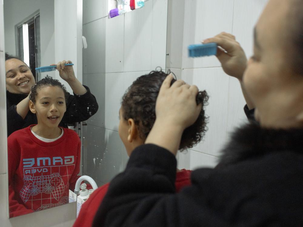 Érica Lacerda de Souza helps her son, Henrique, fix his hair. She says that this is one of the boy's vanities — he wants to make sure his curls look good before heading off to school.