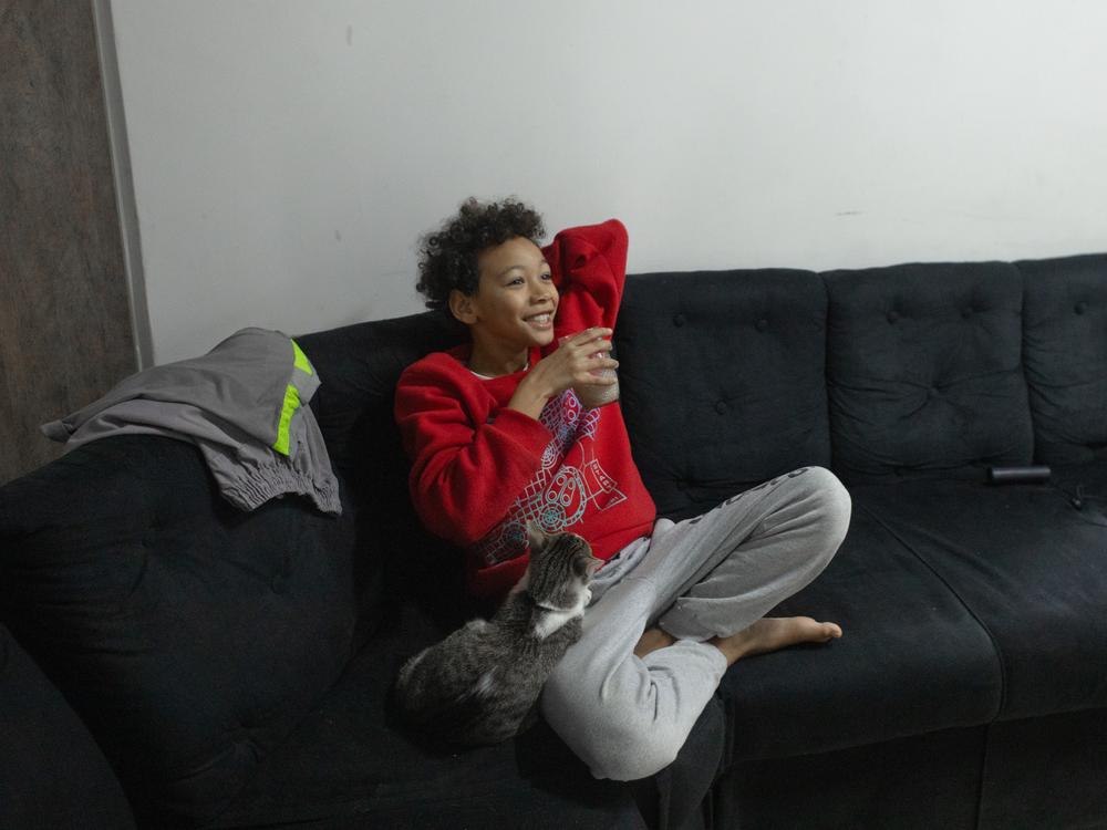 Henrique, son of Érica Lacerda de Souza and Bruce Lee de Souza, has breakfast on the couch in his new home in Guaianazes, São Paulo. When they lost their rental unit during the early days of the pandemic, Henrique went to live with his grandmother.