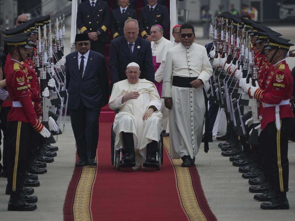 Pope Francis, seated in his wheelchair is welcomed as Indonesian Minister of Religious Affairs Yaqut Cholil Qoumas, center left, walks during an official welcoming ceremony at Soekarno-Hatta International Airport in Tangerang on the outskirts of Jakarta, Indonesia, Tuesday, Sept. 3, 2024.
