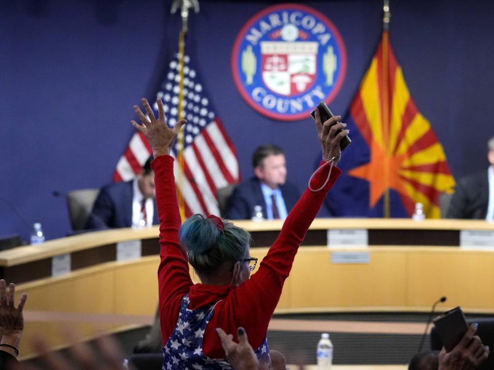 A woman stands in protest as the Maricopa County Board of Supervisors meets to discuss general election results on Nov. 28, 2022, in Phoenix.