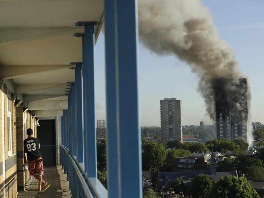 A resident in a nearby building watches smoke rise from the Grenfell Tower building on fire in London on June 14, 2017. 