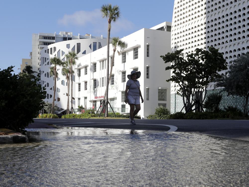 A woman walks along a flooded street caused by a king tide in Miami Beach, Fla., in 2019. So-called sunny day floods are getting more common in many coastal areas as seas rise due to human-caused climate change.