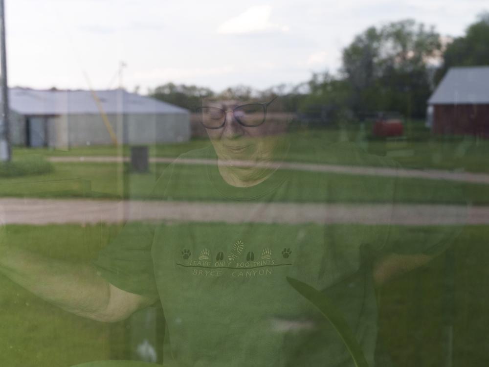 Cindie Haakenson is seen through a window of her home as the family farm is reflected before her on May 21 in Willow City, N.D. Despite a preference to remain at home, Cindie's husband, Sherwood Haakenson, needed to move to a 24-hour long-term care center.