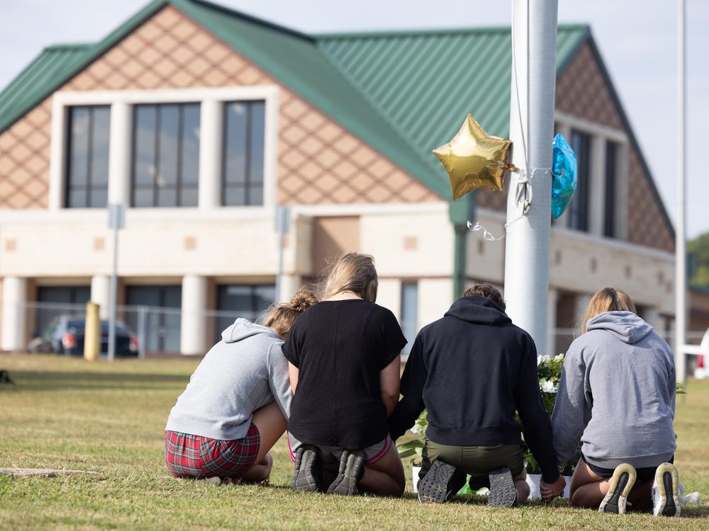 Students kneel in front of a makeshift memorial in front of Apalachee High School on in Winder, Ga., on Thursday, one day after two students and two teachers were shot and killed at the school.