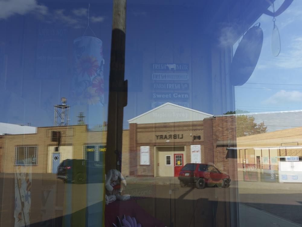 A quiet downtown Glen Ullin is seen reflected in the window of the town's pharmacy on May 24.