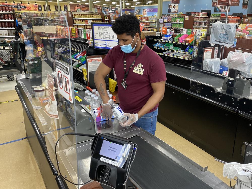 A checkout clerk works behind a plexiglass divider at the ShopRite supermarket in Uniondale, N.Y., at the start of the coronavirus pandemic.