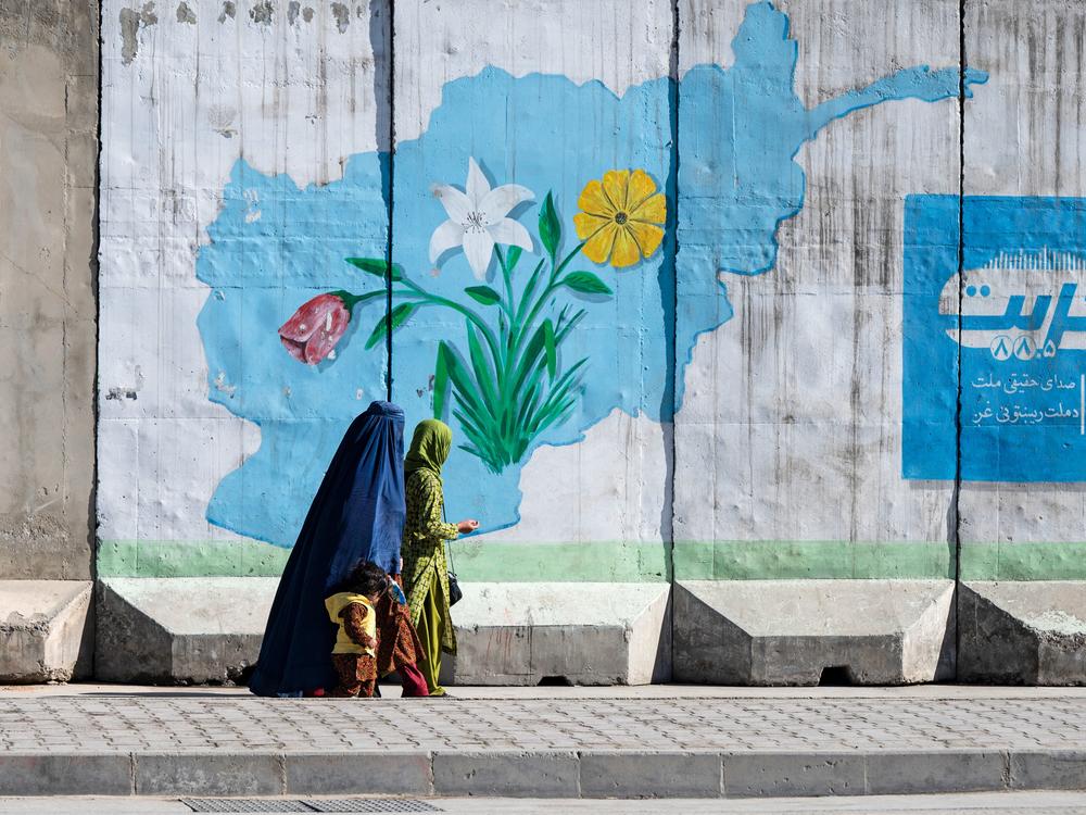 An woman in Kabul walks past a wall mural with a map of Afghanistan. A sweeping new morality law issued by the Taliban requires women to have a male escort on any trip outside home.