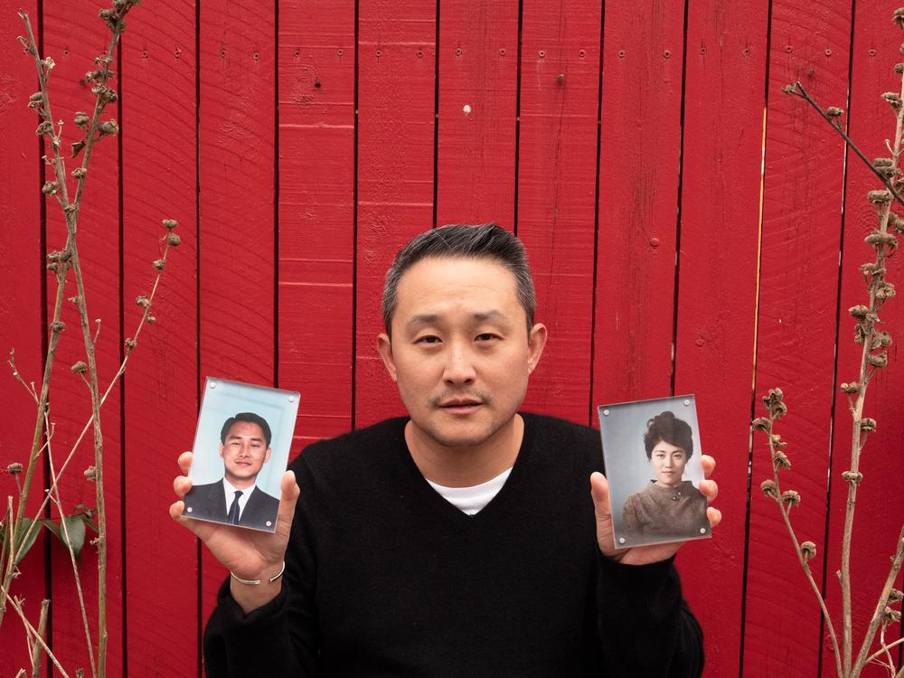<em>Tom Pyun, 46, a Korean American writer, poses for a portrait holding photos of his parents.</em>