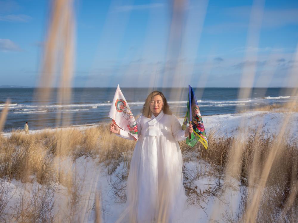 <em>Helena Soholm holds up the five directional flags of Korean shamanism in Dronningmølle, Denmark.</em>