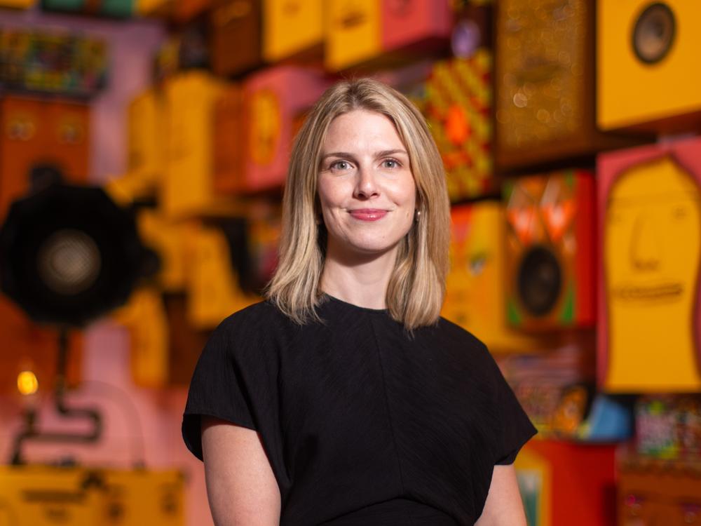 Curator Marina Isgro poses for a portrait in front of a finished portion of the exhibition, with “Gramaphone, 2016” and “ Untitled (92 Speakers), 2019.”