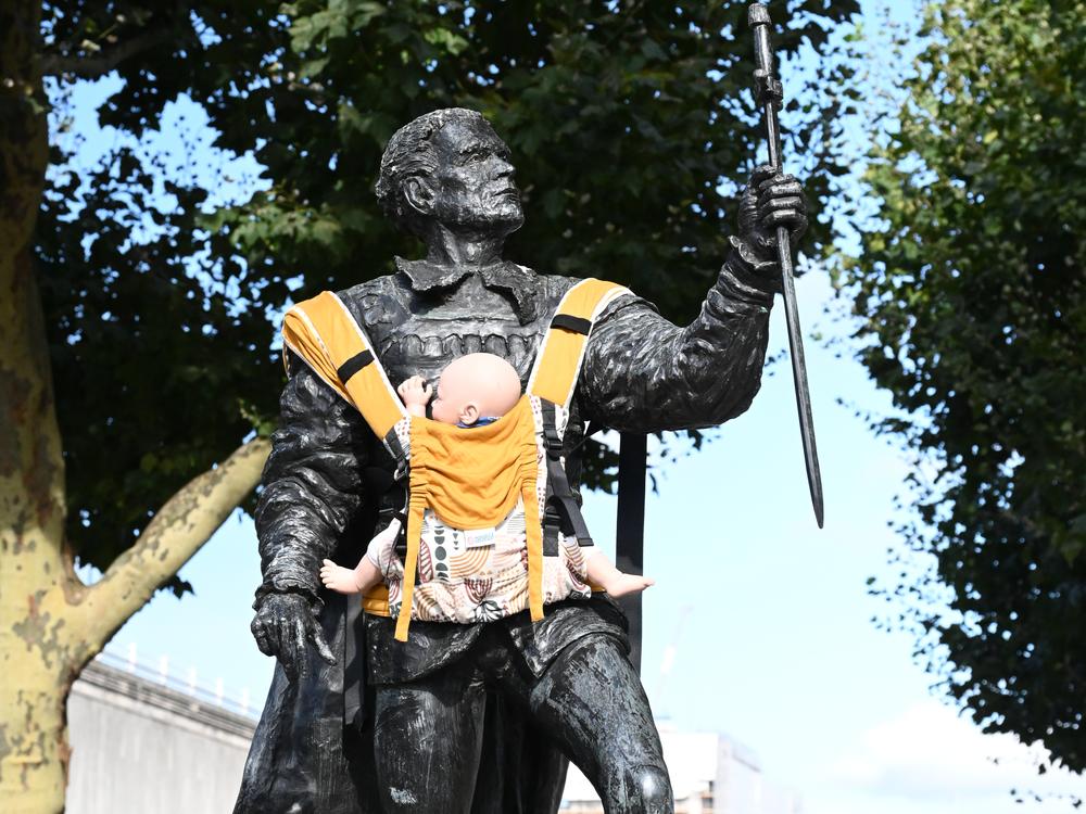 A statue of Sir Laurence Olivier in London with a baby carrier attached to his chest.