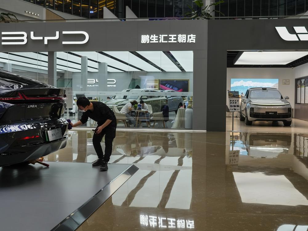 A worker wipes a Rising F7 car model at a floor section selling various Chinese-made electric car brands inside a shopping mall in Beijing, Tuesday, April 4, 2023. (AP Photo/Andy Wong)