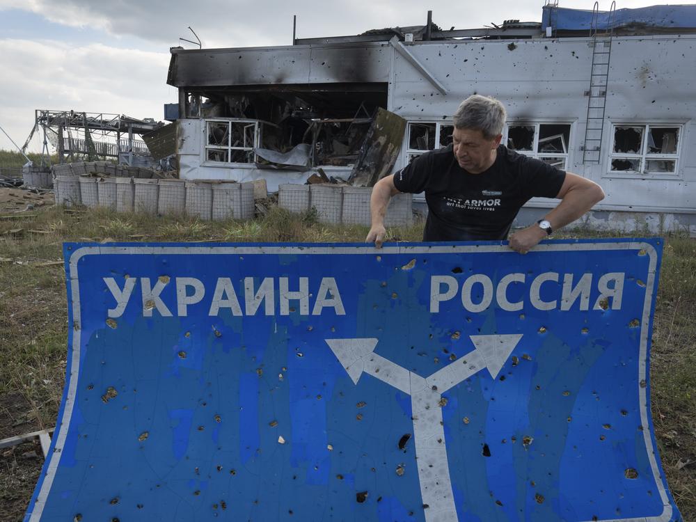Ukrainian historian Yuri Savchuk, the head of Ukraine's World War II history museum, carries a road sign on Aug. 16 in western Russia's Kursk region, an area captured by Ukrainian troops. The sign reads 'Ukraine' to the left, and 'Russia' to the right.
