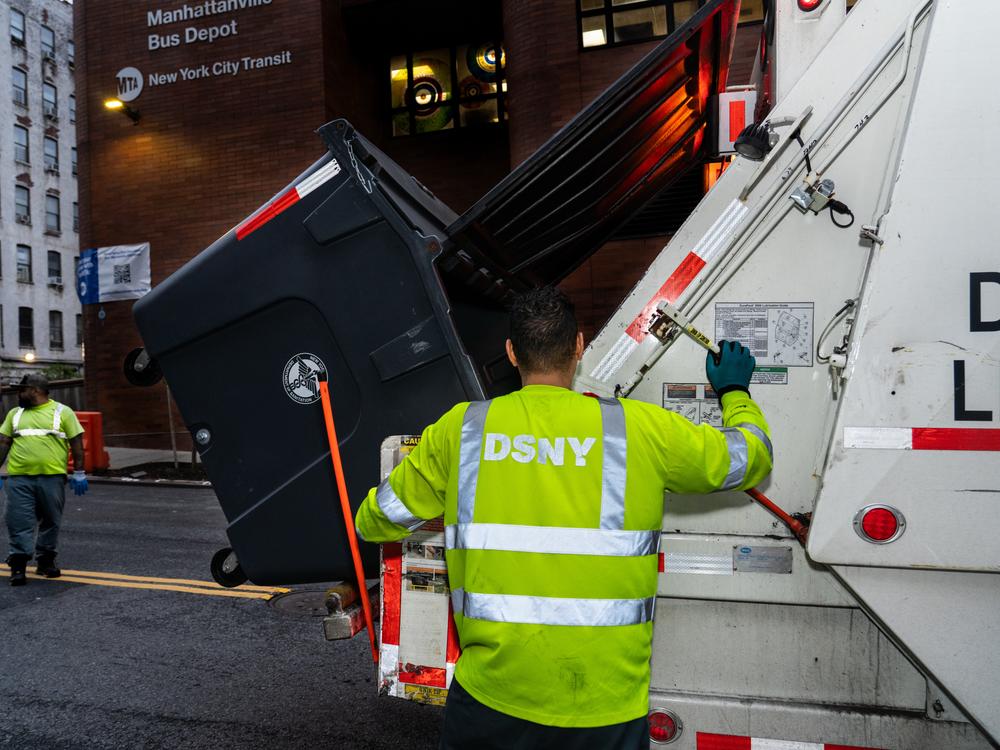 Workers from the New York City Department of Sanitation collect trash deposited in large bins used in West Harlem's pilot program. The large bins can be picked up by the collection trucks, which mitigates certain risks for workers, like being cut by broken or sharp objects thrown out.