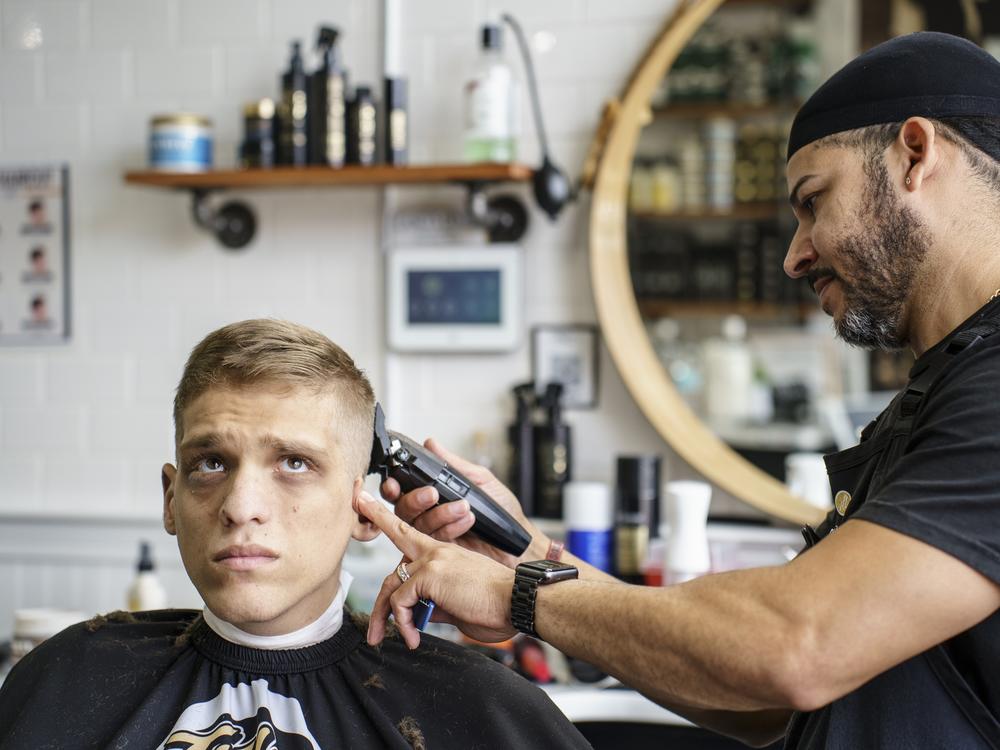 August 22, 2024, Natick, MA.<br />
Jason Mazzola getting his haircut by Jose Nieves at Title City. 