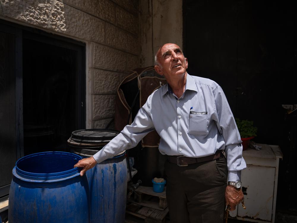 Samhan Shreiteh walks around his house to show the new tanks he uses to gather water. Shreiteh has to buy water from a water delivery service — something he’s never had to do before — which the family stores in tanks and buckets outside the house. For this service, he says he’s paying five times as much for water as he was before Oct. 7.