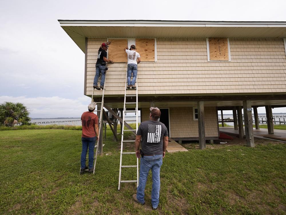 Jerry McCullen, top of ladder left, and Carson Baze, top of ladder right, put plywood over the windows of a house ahead of Hurricane Helene, expected to make landfall Thursday evening, in Alligator Point, Fla., Wednesday, Sept. 25, 2024. (AP Photo/Gerald Herbert)