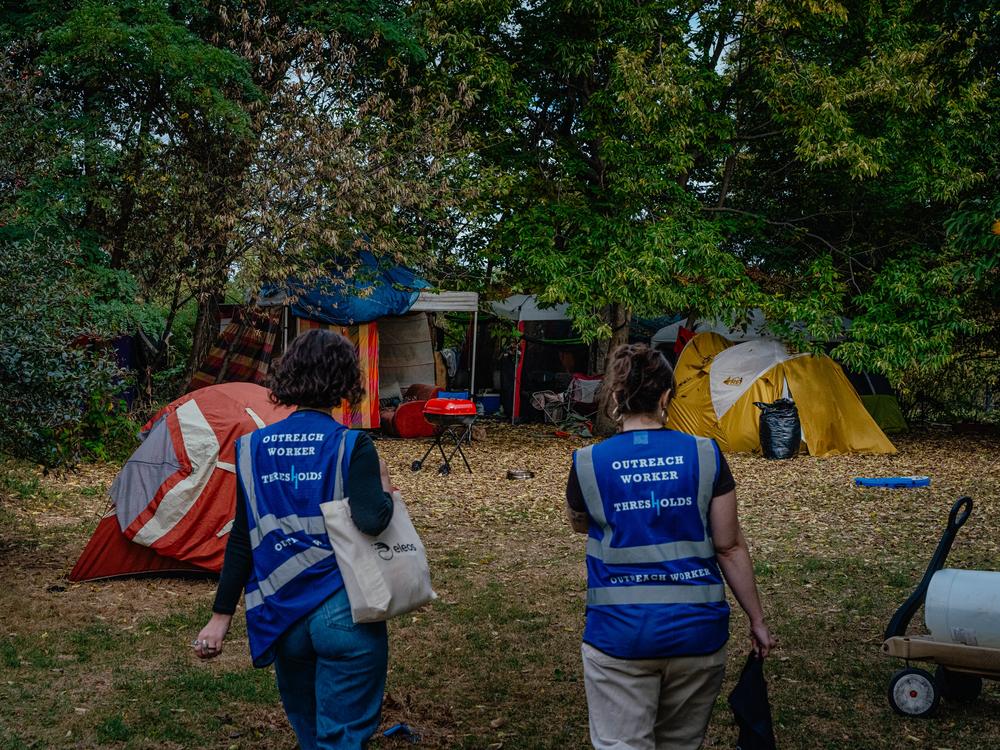 Lillian Risser, left, and Sophia Loveland, right, approach an encampment in Humboldt Park on Sept. 23 in Chicago. Risser and Loveland are outreach workers for Thresholds, a mental health care provider in Illinois that works to move people out of encampments into more permanent housing. 