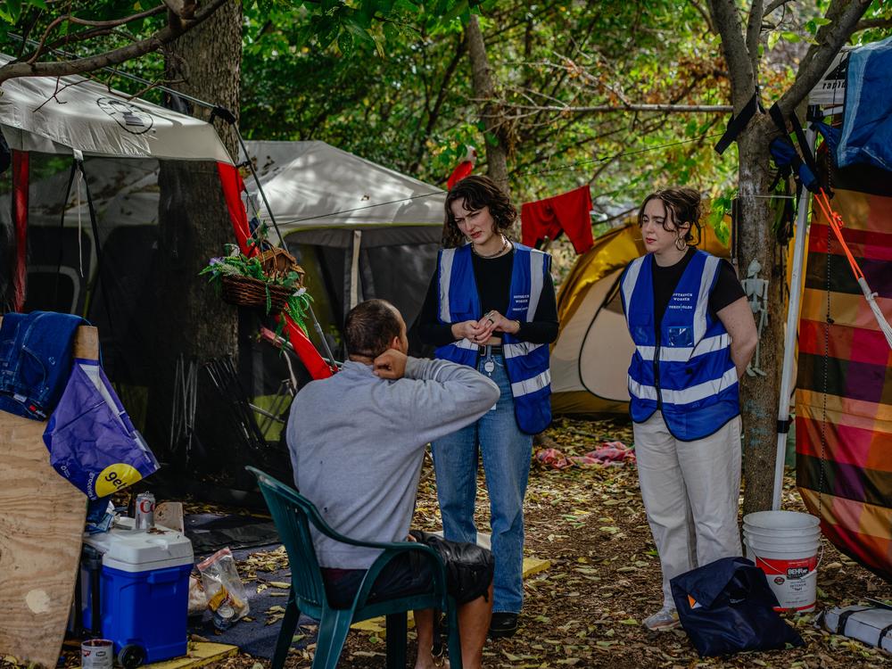 Thresholds outreach workers Risser, left, and Loveland, right, speak with Julius Rodriguez, who is living in a tent encampment in Chicago's Humboldt Park. The day they visited, the workers called medical help to take Rodriguez to a hospital for pain.