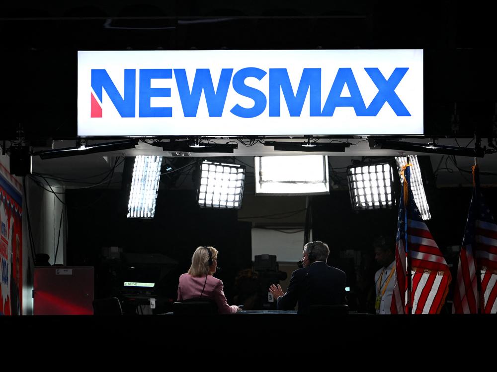 News anchors work at Newsmax's booth during the 2024 Republican National Convention in Milwaukee, Wisconsin. The network has settled with voting-tech company Smartmatic, which accused it of defamation following the 2020 presidential election. 