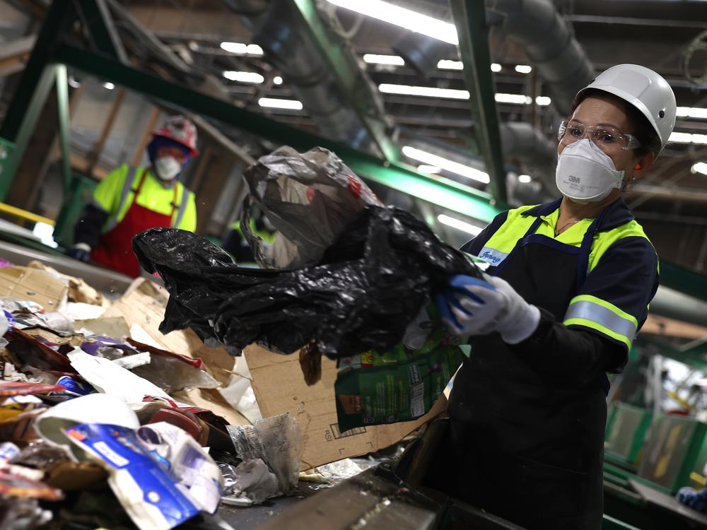 California is banning single-use plastic bags at grocery stores and other retailers, after an earlier ban was blamed for making the waste problem worse. Here, a worker pulls a plastic bag from a conveyor belt as she sorts through materials at a recycling center in San Francisco.