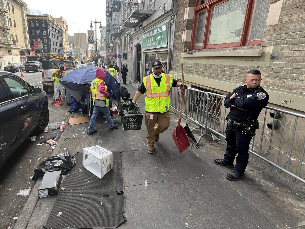 San Francisco police officers keep an eye on city workers as they sweep unsanctioned tents and belongings from a street in the Tenderloin.
