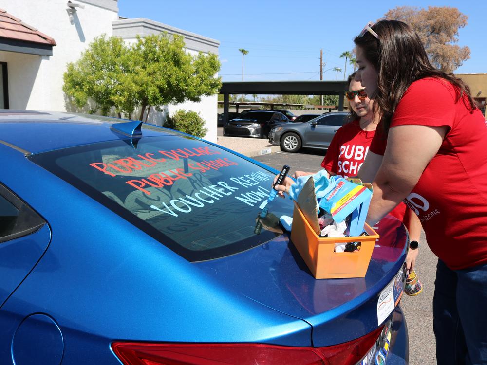 Jen Senatore, right, and Tyler Kowch with Save Our Schools, a public education advocacy group in Arizona, paint cars outside of a local Democratic Party office in Phoenix. The paint reads, 