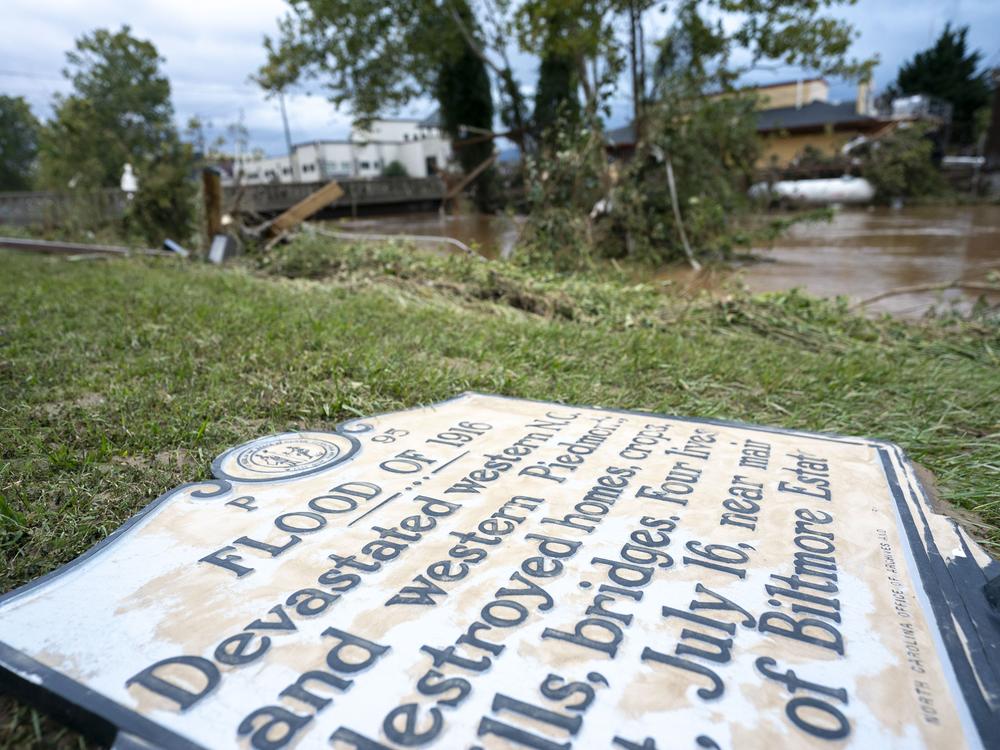 A sign commentating the flood of 1916 lies on the ground next to a flooded waterway near the Biltmore Village in the aftermath of Hurricane Helene on Sept. 28, 2024.