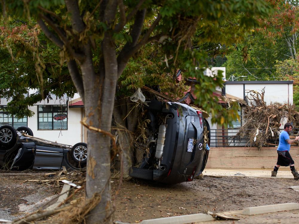 A man walks past damaged vehicles at the Biltmore Village across from the Biltmore Estate in the aftermath of Hurricane Helene on Oct. 1 in Asheville, N.C.