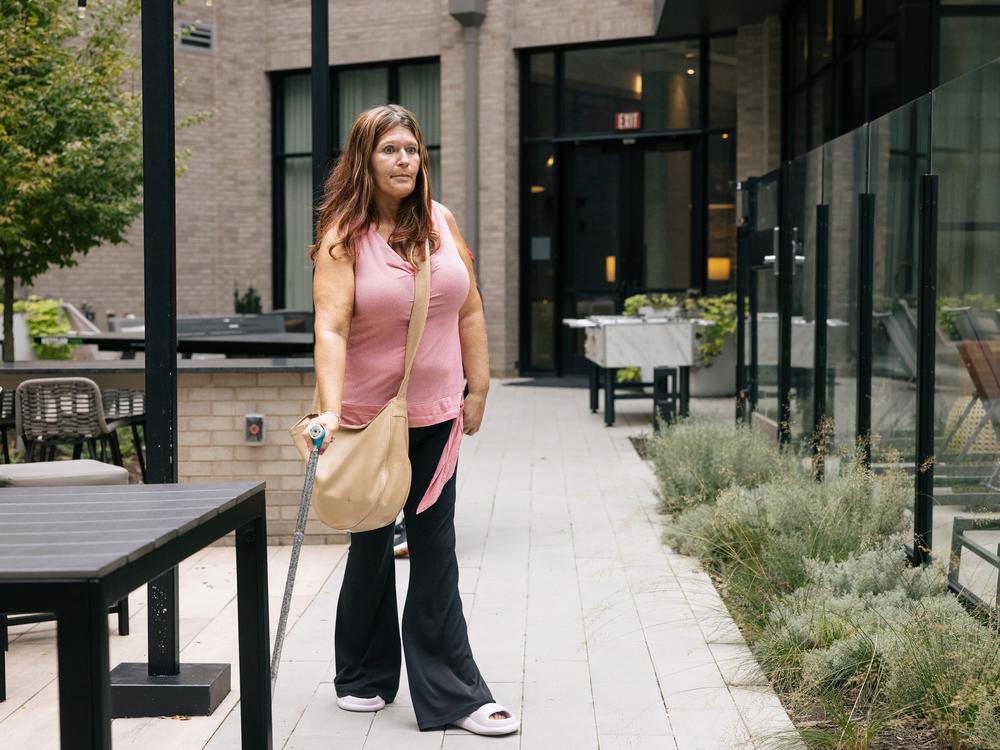 Christina Cooley, who requires a cane to walk and is on disability, walks through the courtyard of The Laureate, where rents typically range from about $1,335 for a smaller one-bedroom — far below the county median — to $3,885 for a larger two-bedroom.