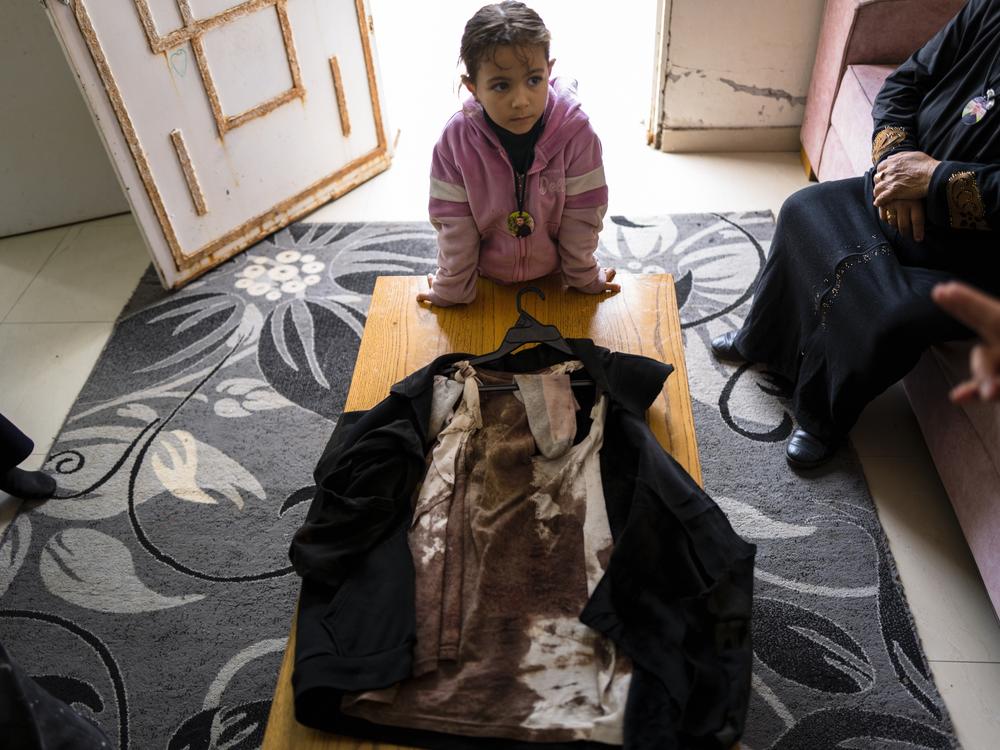 Ahmed Assi’s 5-year-old daughter, Jenna, looks at his bloodied clothes. She wears a necklace with a picture of her dead father.