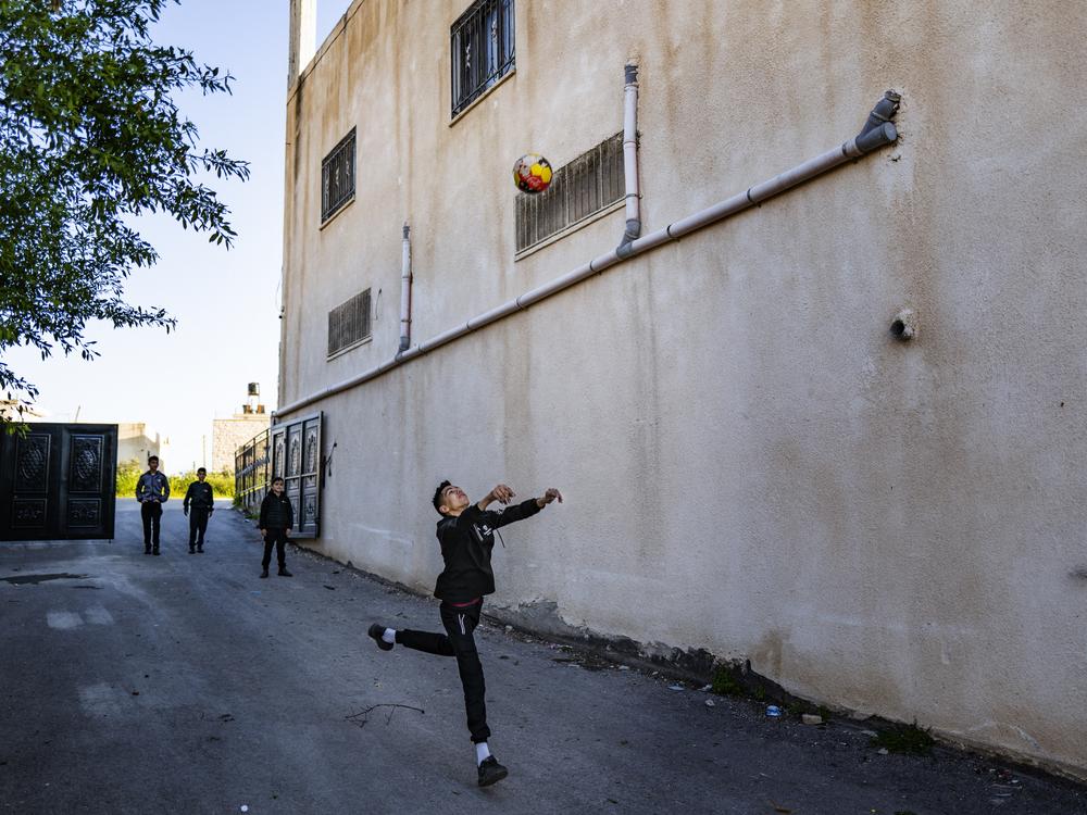 Noor playing with a soccer ball outside his home.