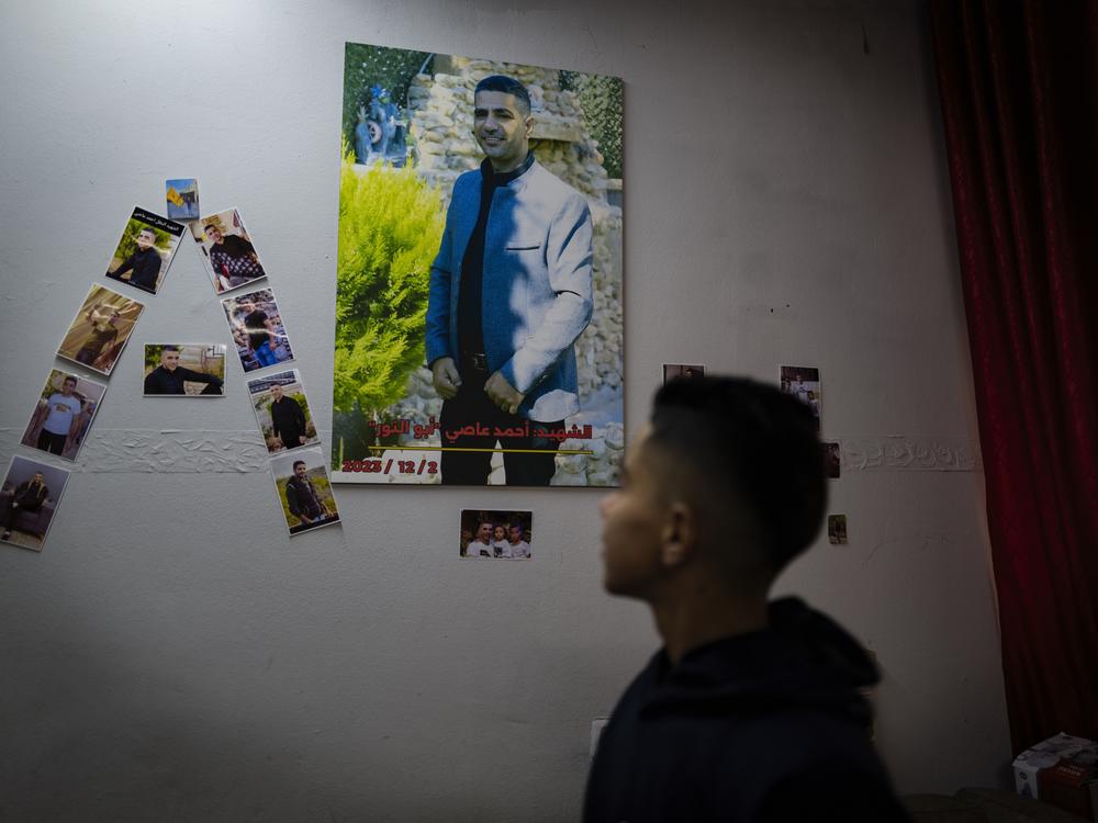 Noor Assi looks at a photo mural of his slain father, Ahmed, in their family home.