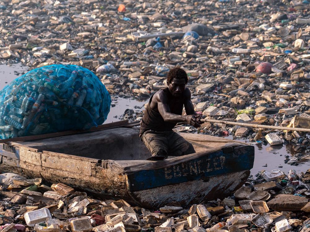 A man in a canoe pulls toward the banks to recover more recyclable plastics. E-waste dumping takes a heavy environmental toll, often degrading the local water supply.