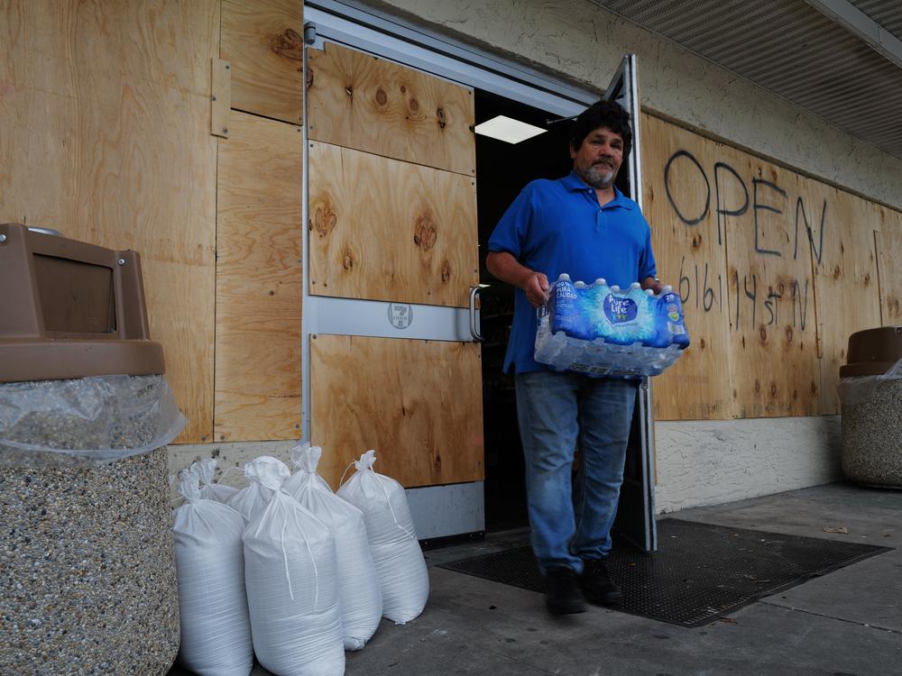 People walk in and out of a boarded-up 7-Eleven on Tuesday in St. Petersburg, Fla., as the state prepares for the arrival of Hurricane Milton, which is expected to make landfall late Wednesday.