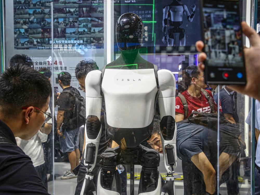 Visitors look at Tesla's humanoid robot Optimus at its exhibition booth during the World Artificial Intelligence Conference (WAIC) in Shanghai on July 5, 2024. Optimus, a featureless humanoid robot, can walk and fold laundry. Musk has argued it could eventually learn to do almost anything a human can do.