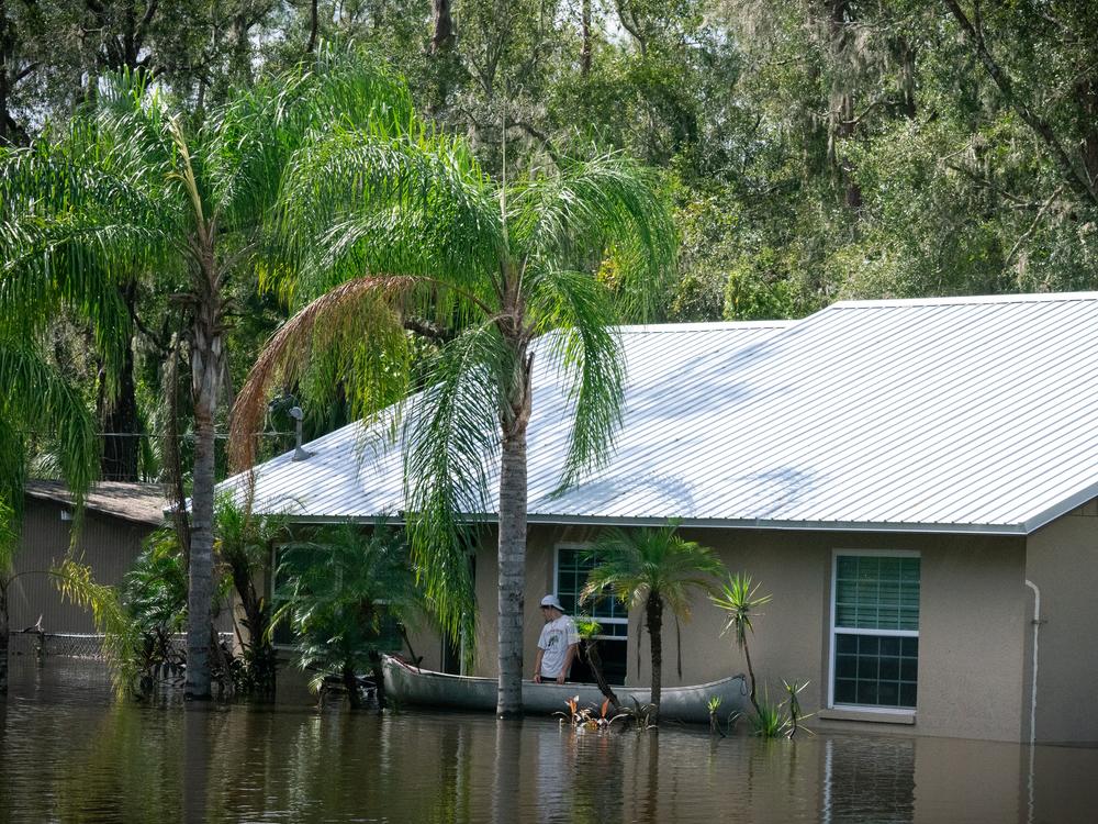 In a flooded Valrico neighborhood, a man waits outside of a home after paddling two others, who entered through the window, up to it.