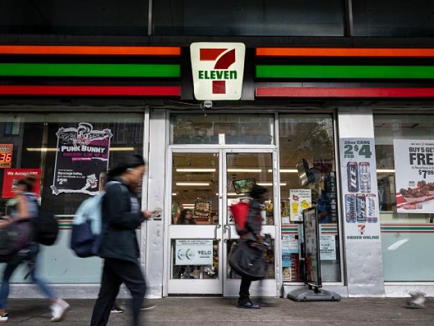 People walk past a 7-Eleven convenience store in New York City on Wednesday. The company plans to shut down 444 stores across North America to recoup costs lost to inflation, a drop in store traffic and declining cigarette sales.