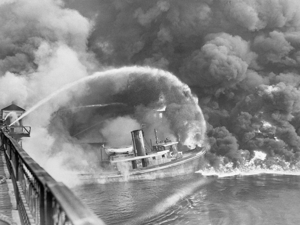 Firefighters stand on a bridge over the Cuyahoga River to spray water on the tug Arizona as a fire, started in an oil slick on the river, engulfs docks in Cleveland on Nov. 1, 1952.