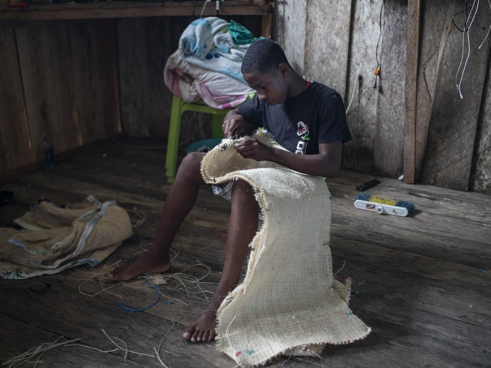 A boy designated to be one of the Manacillos sews his costume for Holy Week on March 29, 2024, in Juntas, Buenaventura, Colombia.