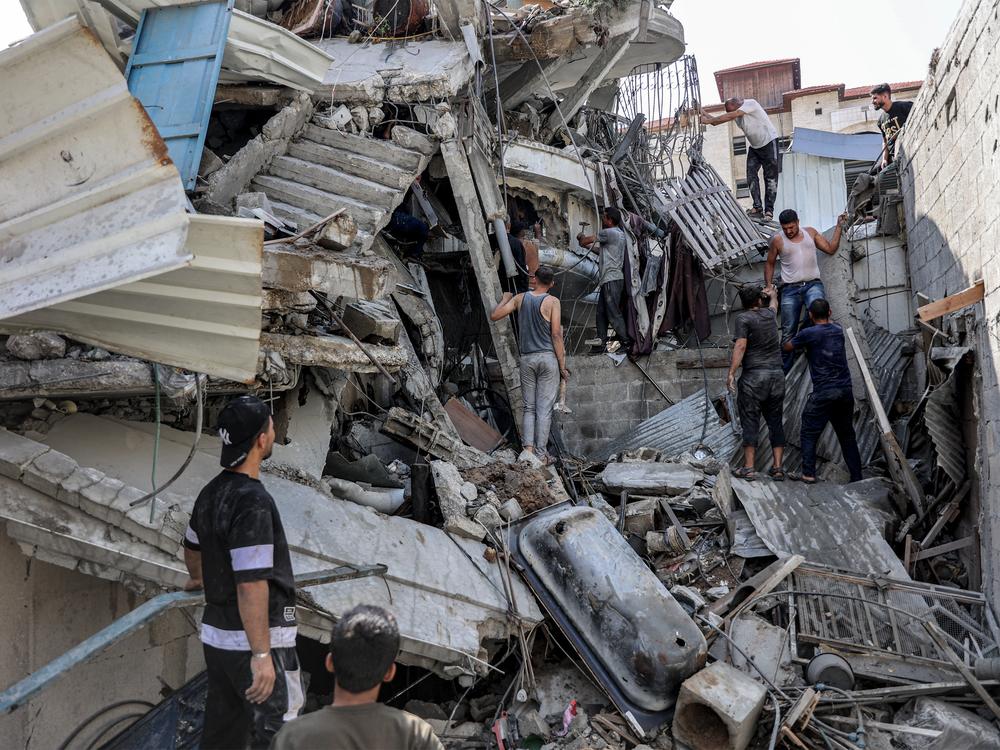 People gather outside a collapsed building as they attempt to extricate a man from underneath the rubble following Israeli bombardment in the Saftawi district in Jabalia in the northern Gaza Strip on October 15.