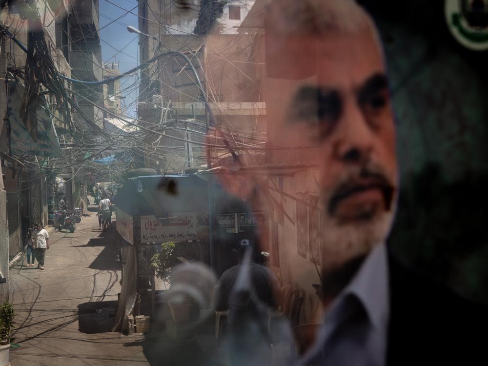 People are reflected in a window displaying a poster of Hamas leader Yahya Sinwar in the Palestinian camp of Bourj al-Barajneh, on Aug. 8, in Beirut.