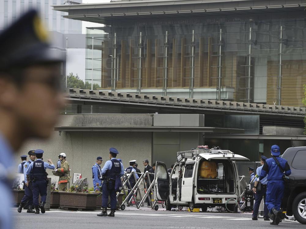 Police officers work near a vehicle, center, which was stuck against a barricade near the prime minister's office, background, in Tokyo on Saturday.