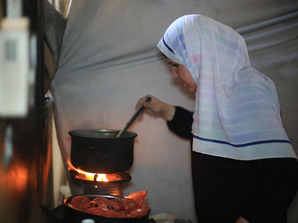 In the shelter where her family stayed this summer, Suad Ali Al-Nidr cooks mulukhiyah, a soup made from jute leaves, for her kids. 