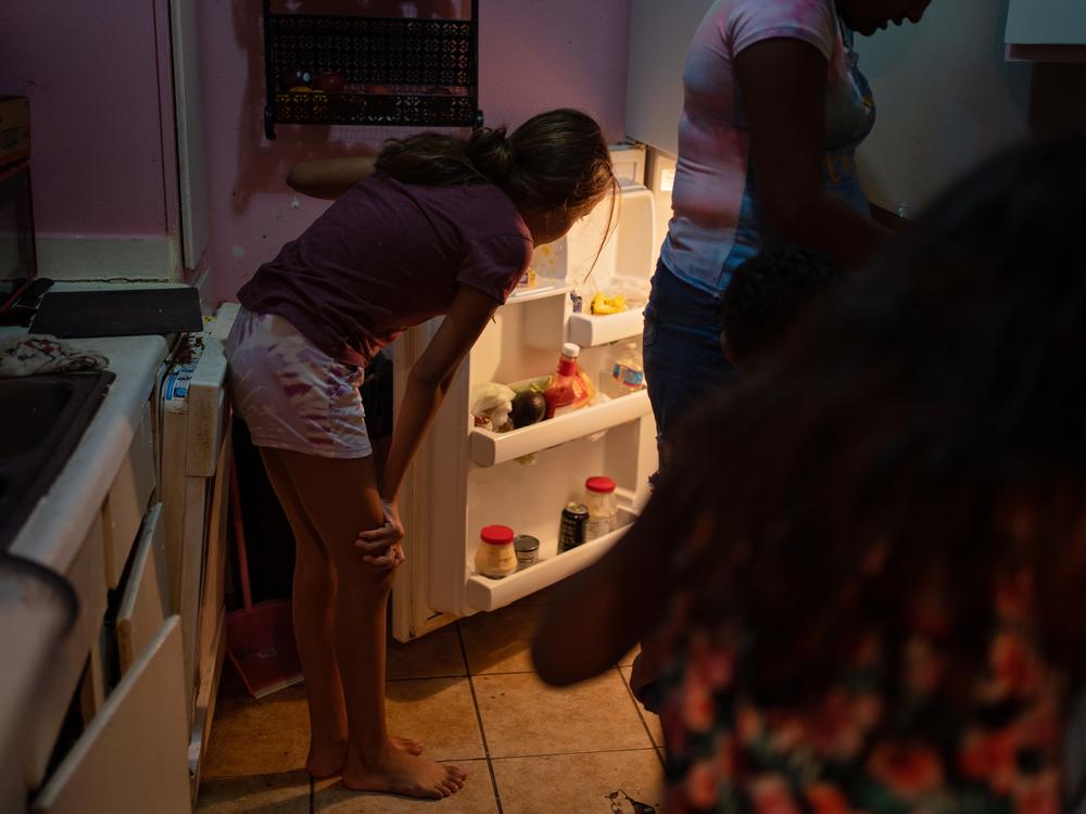 Emilia Lopez's 12-year-old daughter looks into the family's refrigerator. For occasional treats, Lopez uses the government aid she receives to buy ice cream and chips. Most of the time, however, she makes it a priority to purchase essential items.