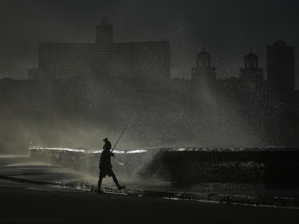 A person fishes along the boardwalk as waves crash during a power outage in Havana, Monday, Oct. 21, 2024.