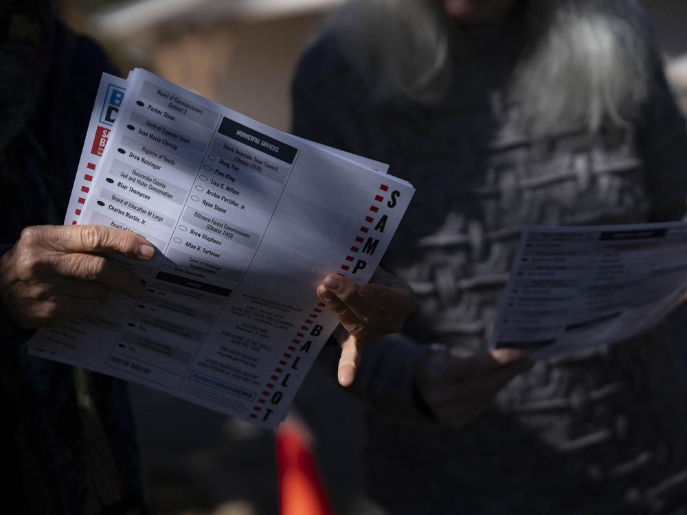 A woman holds a sample ballot on the second day of early voting at a polling station, Oct. 18, in Fairview, North Carolina. Despite concerns about early voting access after Hurricane Helene, many local officials reported record turnout for early voting, like in nearby Yancey County.